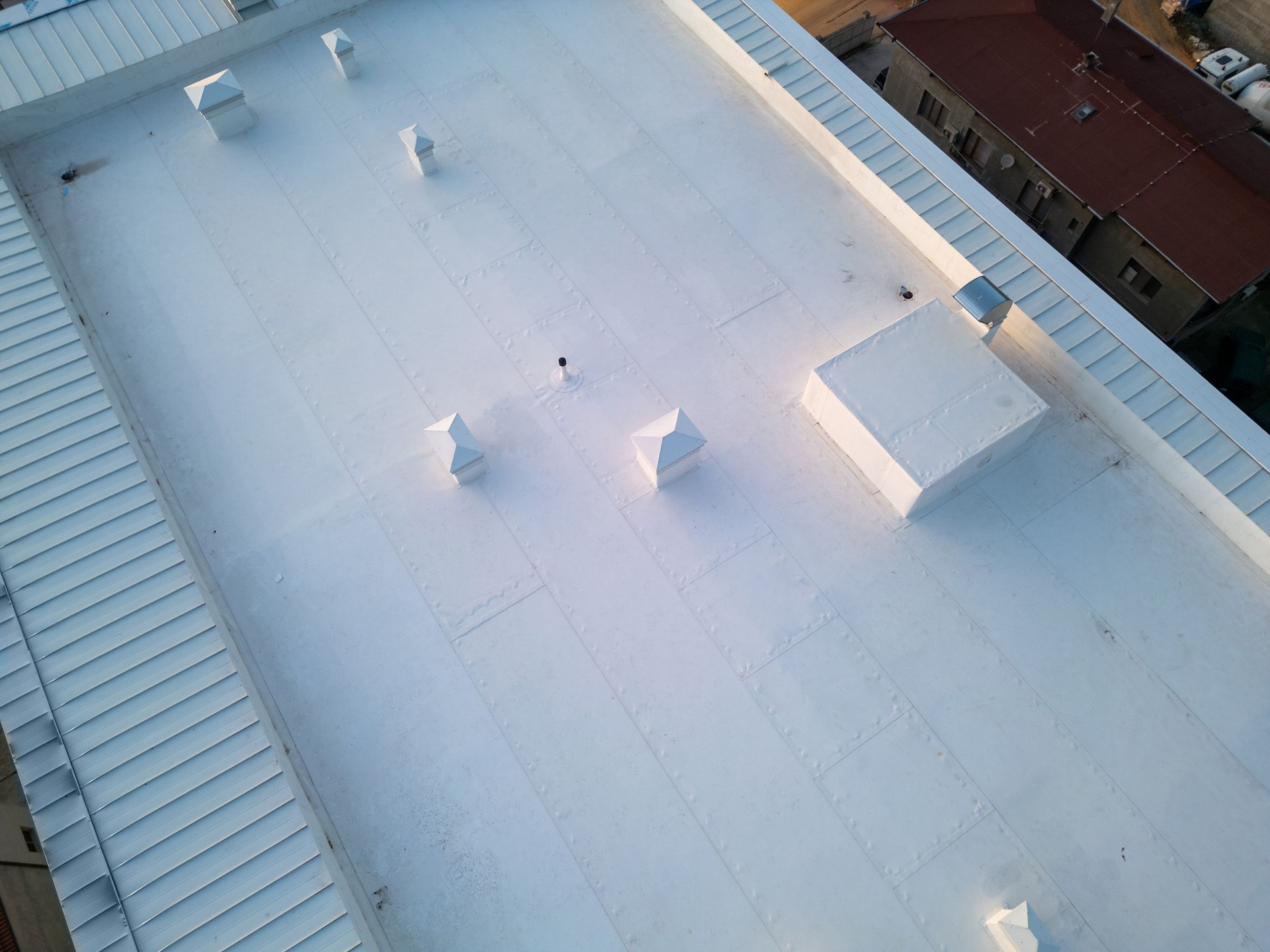 Aerial view of a white industrial rooftop showcasing a clean, minimalistic design with multiple vents and structures. The symmetrical layout and geometric patterns create a modern architectural aesthetic, captured from a drone perspective